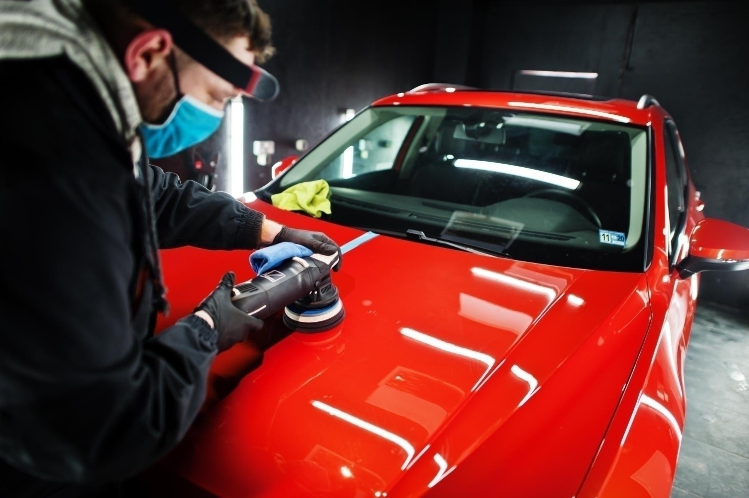 car detailing concept man face mask with orbital polisher repair shop polishing orange suv car