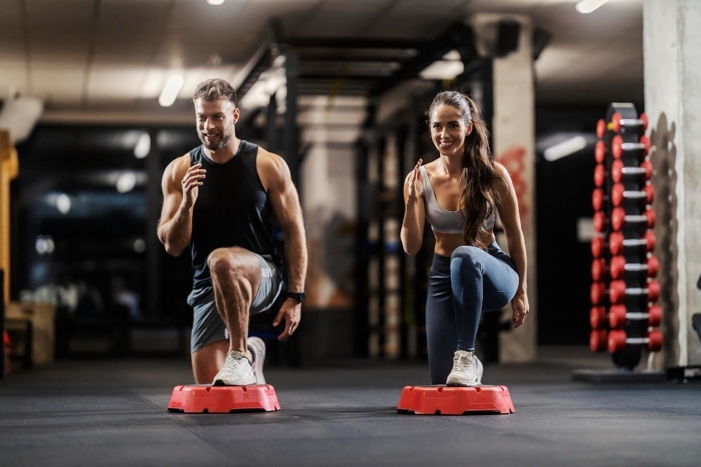 A fit couple is doing exercises for gluteus and legs in a gym