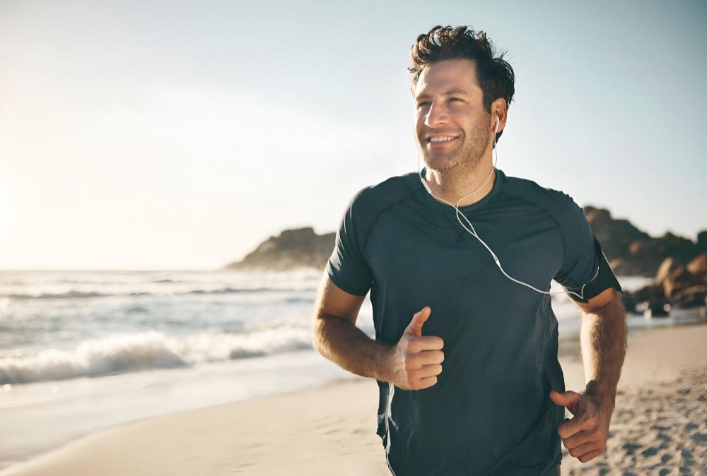 Active fit and healthy man jogging on a beach while listening to music on earphones