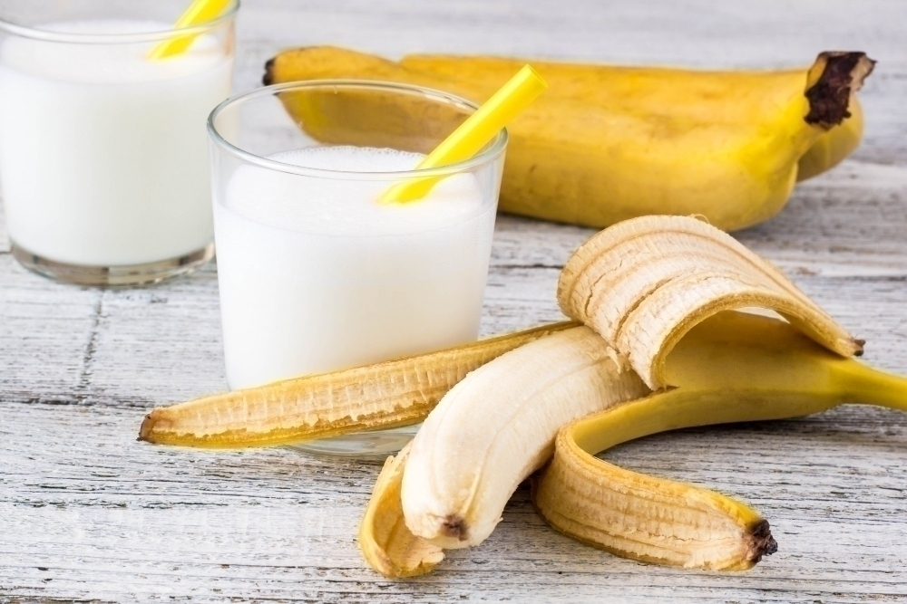 Banana cocktail and fresh bananas on wooden background