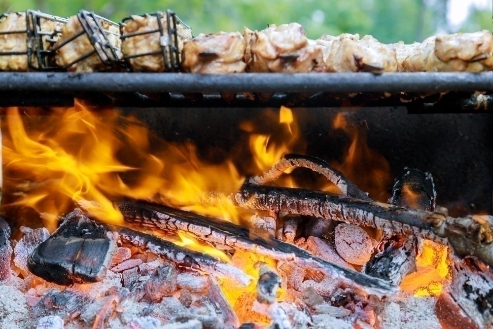 Charcoal barbecue grill with flame and cooking meat in soft focus.