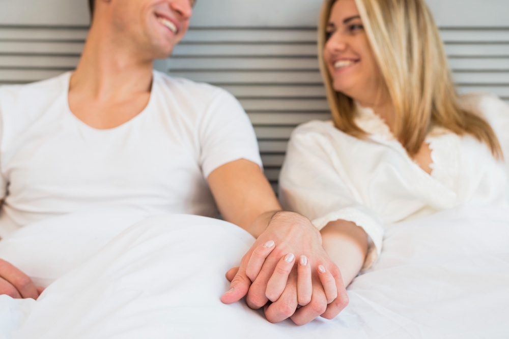 Cheerful man holding hand of young woman in bed