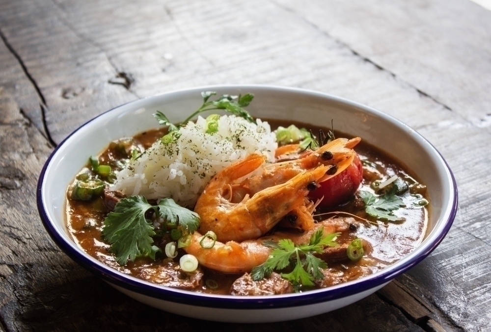 Close shot of soup with shrimps rice and vegetables leaves in a bowl on a wooden surface