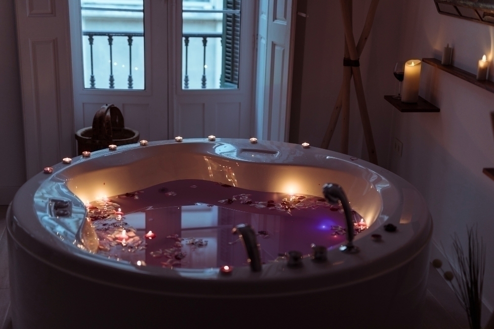 Flower petals on water in spa tub with burning candles on edges