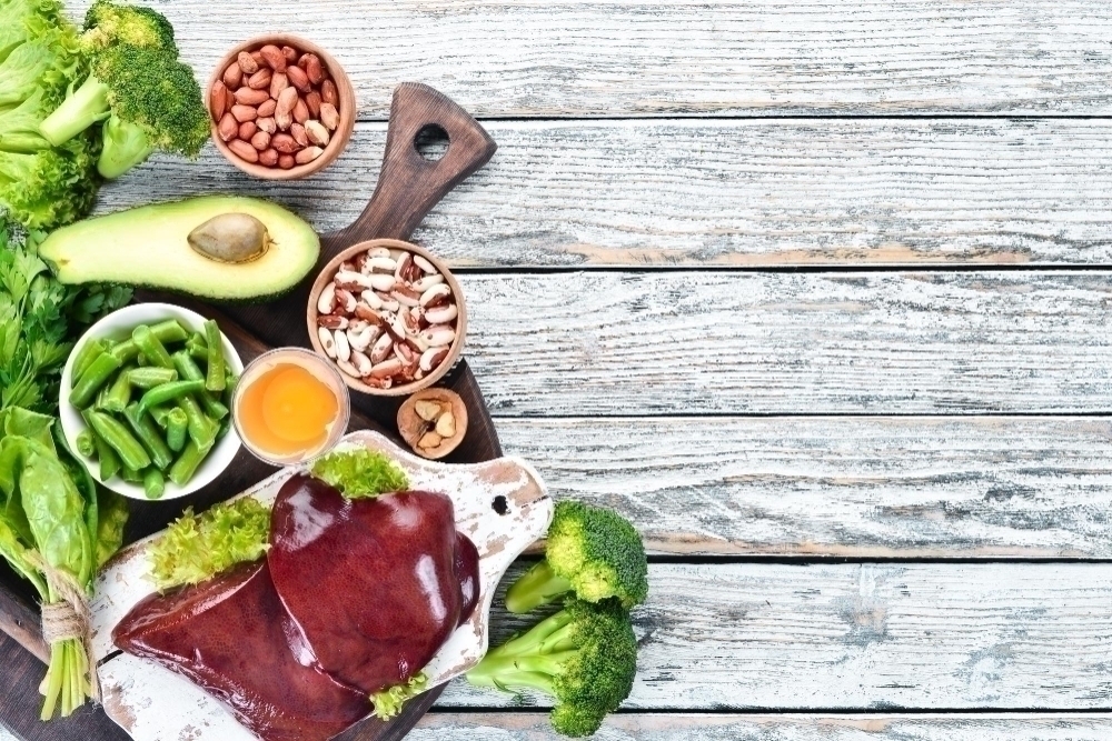 Foods that contain natural vitamin B9 Liver avocado broccoli spinach parsley beans nuts on a wooden background
