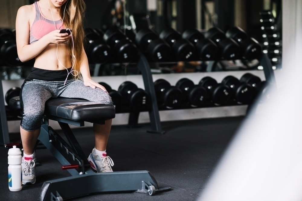 Girl with phone sitting on exercise bench in gym