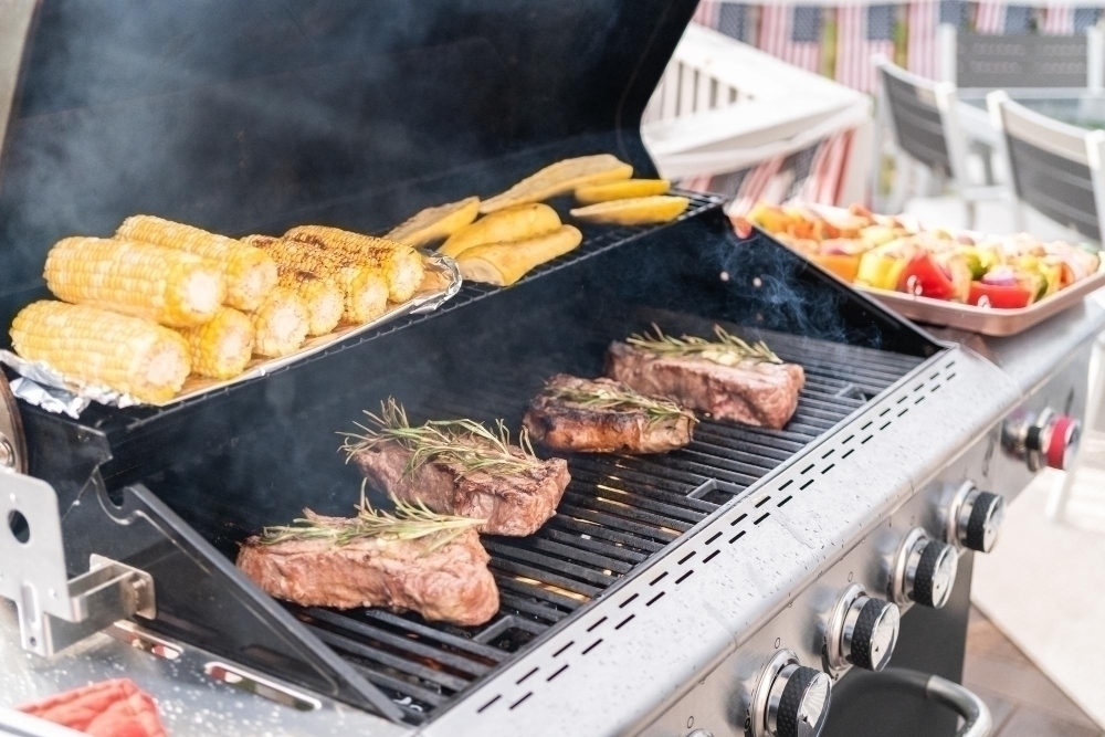 Grilling New York steak with a slice of butter and rosemary on an outdoor gas grill.