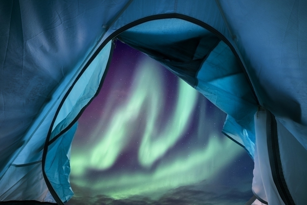 Inside of blue tunnel tent camping with aurora borealis flying in the night sky