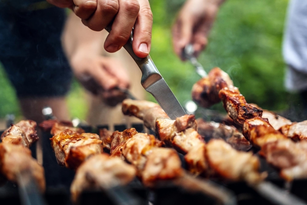 Man hands trying barbecue delicious grilled meat with knife preparing at the nature picnic with pork