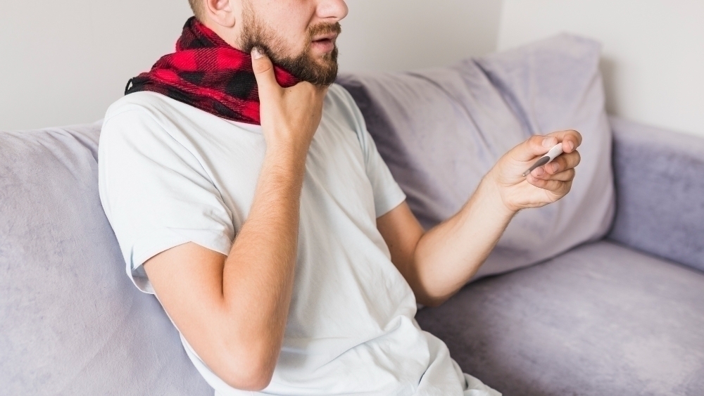 Man med scarf haller om halsen o en termometer