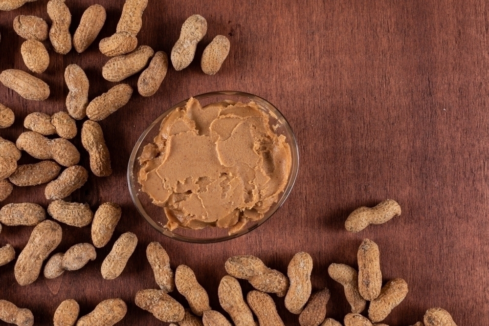 Peanut butter surrounded by raw peanuts on wooden with copy space
