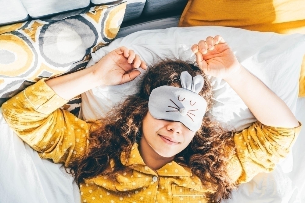 Portrait of smiling young woman lying in bed wearing a sleeping mask