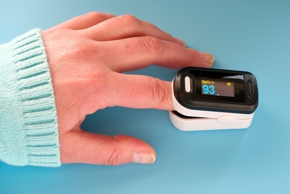 Pulse Oximeter portable digital device to measure person oxygen saturation device on female hand blue mint wall