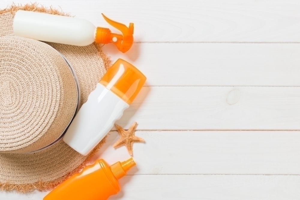 Sunscreen bottles with starfish and sunhat on white wooden table with copy space. Travel healthcare accessories top view