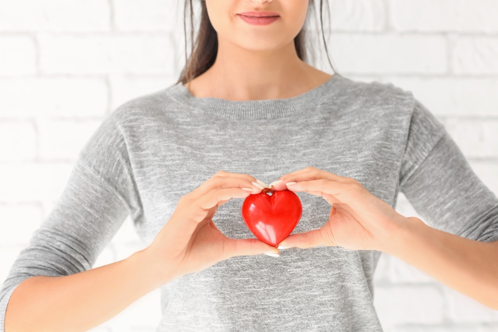 Woman holding red heart on light surface Q10 supplement info