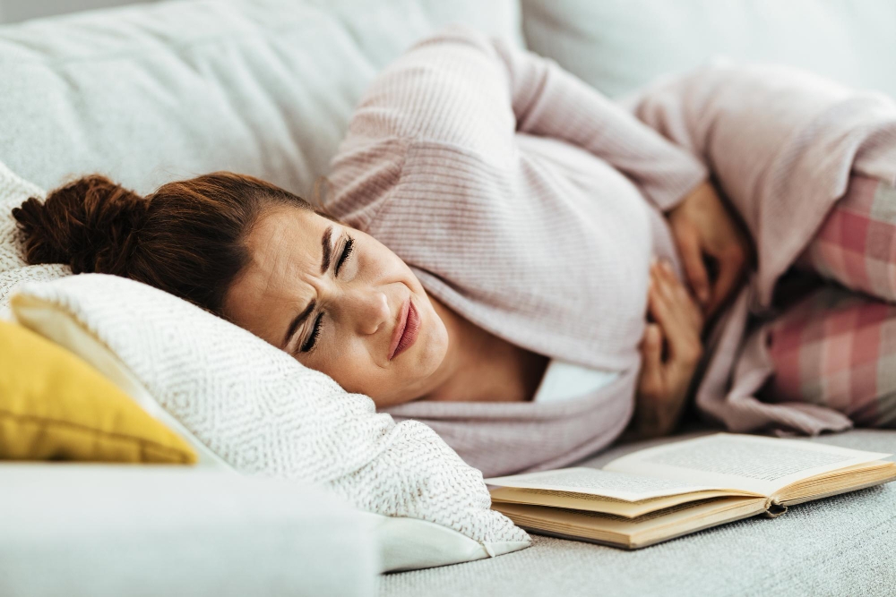 Young woman with PMS feeling pain in her abdomen while lying down on sofa at home