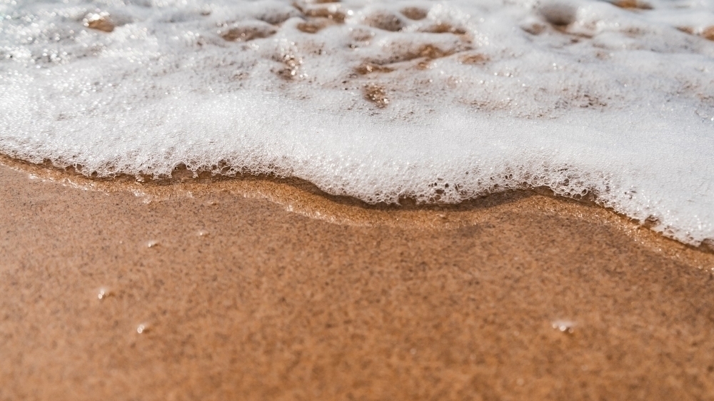 high angle shot foamy waves coming towards sandy beach