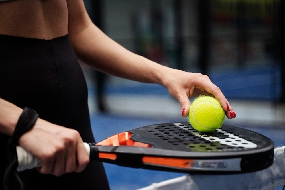 kvinna rulalr padelboll mot padelracket