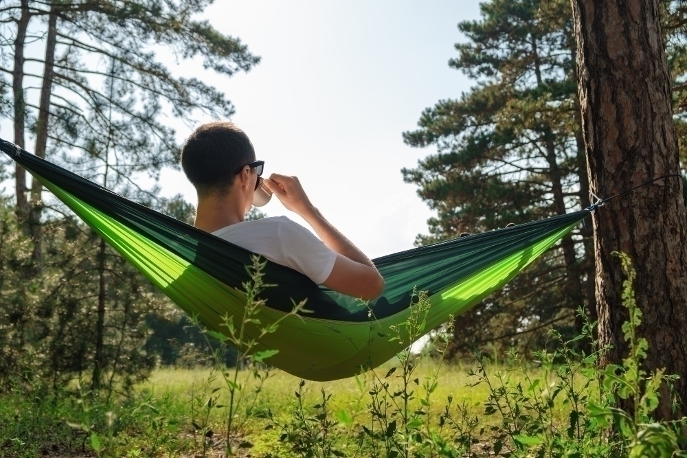 man dricker kaffe i hangmatta i skogen