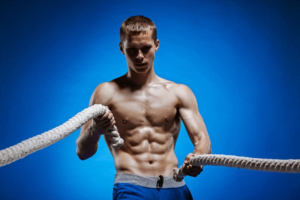 shredded young man with ripped torso and a rope on blue